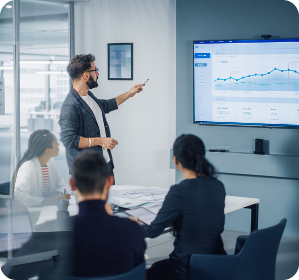 employees having a discussion in a conference room while looking at a graph on a large wall-mounted screen